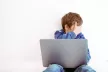 A scared young boy covering his eyes at the laptop screen