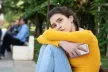 A teenage girl looking sad, bracing herself and holding a smartphone