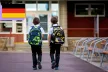 Two young children facing away from the camera and walking towards their school with matching black and green backpacks.