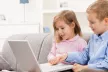 Two young children, sat on a sofa, using a laptop