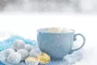 Hands holding a cup of warm beverage in the snow.