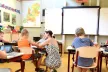Students in a classroom setting, with one being helped by a teacher