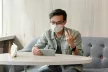 Man wearing a facemask,seated at a table using a mobile device