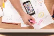 Birds eye view of a desk with hands, with papers, pens and a mobile device