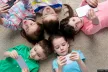A group of five children all looking at smartphones while lying down on a carpet