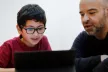 A young boy looking at a computer screen with his parent