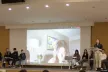 People on stage with a screen showing a woman in the background