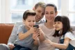 A family of four (mum, dad, boy, girl) all looking at a smartphone sitting on the sofa
