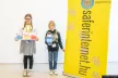 Two children standing next to a yellow banner with the Hungarian SIC website saferinternet.hu