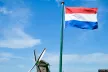 The writing "#SID2023" in the foreground of a Dutch flag waving next to a green windmill.