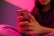 A female teenager watching her phone under a pink light.