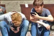 Two boys sitting side by side and using their phones