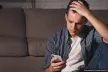 A young man stares at his phone screen in distress