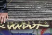 The detail of a hand and hips of a person sitting on a wooden bench.