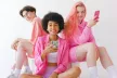 Three diverse teenagers dressed in pink holding smartphones and smiling at the camera
