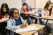 A group of three students in a classroom, two of which are holding and looking at smartphones
