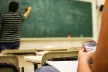 A student checking their phone while the teacher is writing something on a board