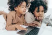 Two young children laid down using a laptop