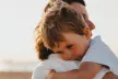 A sad young child being held by a parent or carer
