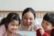 A mother and her two children playing on a tablet and laughing