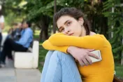 A teenage girl looking sad, bracing herself and holding a smartphone