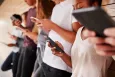 A group of five young people all holding their own smartphone and looking at it.