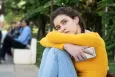 A teenage girl looking sad, bracing herself and holding a smartphone