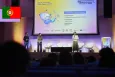 Three speakers on stage in front of a screen presenting the creation of Portugal’s Linha Internet Segura (LIS) chatbot.
