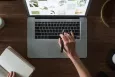 Birds eye view of a laptop on a desk, with a hand typing