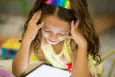 A young girl with her hands on her face, looking at her tablet.