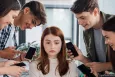Unhappy girl unhappy with teenagers standing around her with  smartphones
